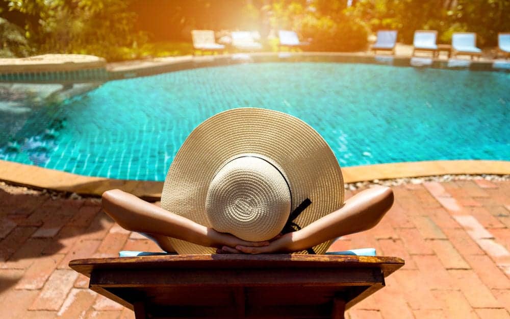 Bikini woman sexy in pool relaxing young asian beautiful female resting in vacation on summer season with hat at resort swimming pool edge with chair beach on side