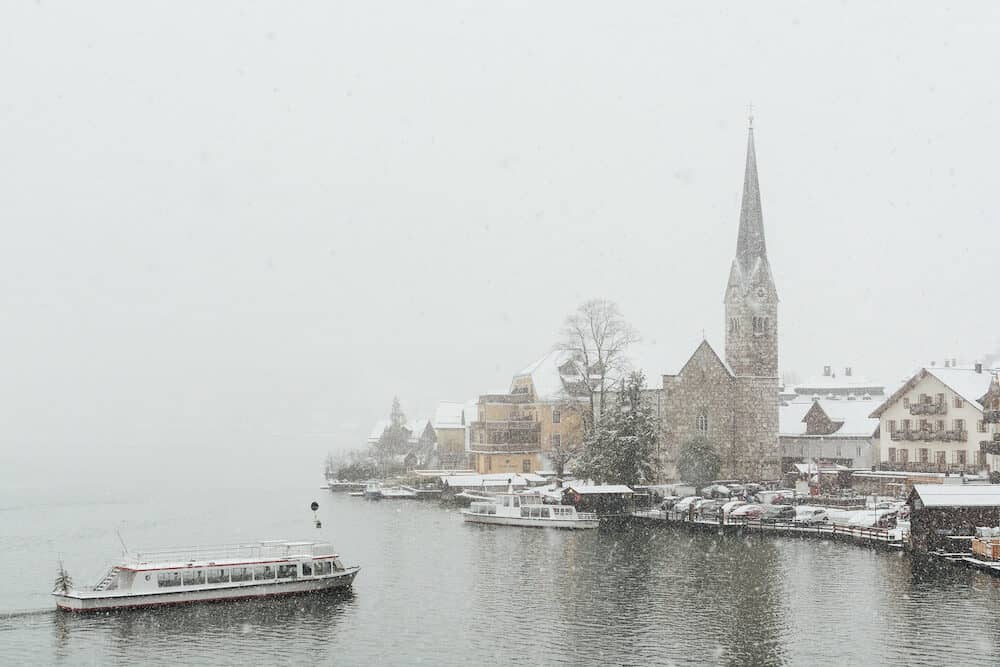 HALLSTATT, AUSTRIA - Lake ferry approaching Evangelische Pfarrkirche and old town during snow storm.