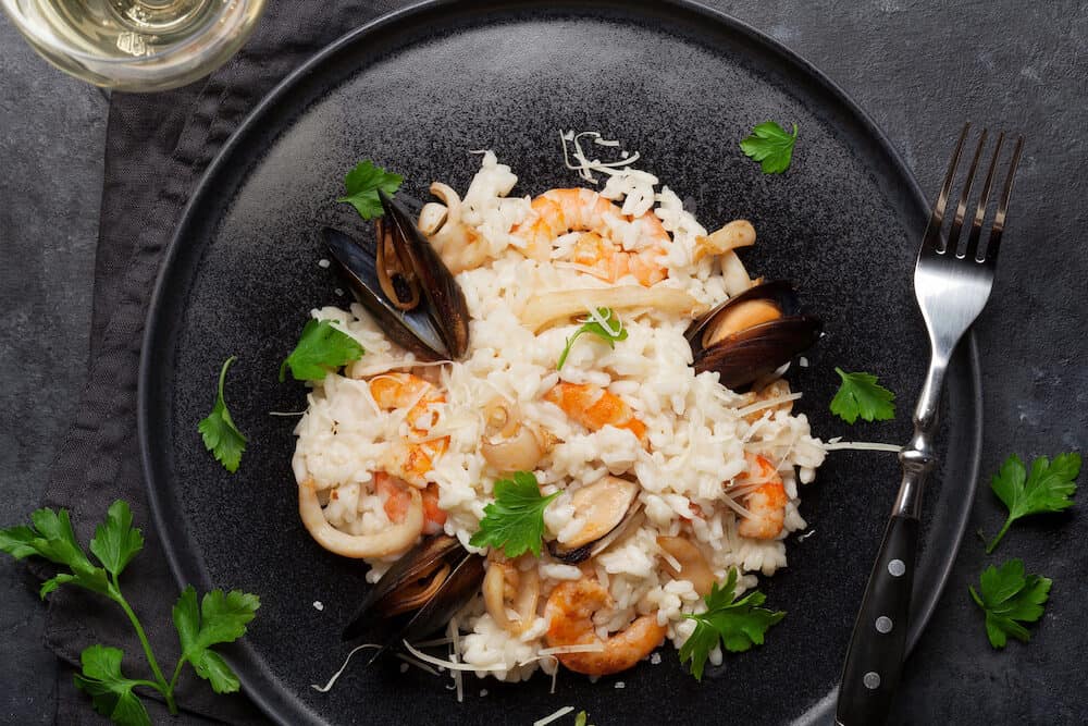 Delicious seafood risotto with shrimps, prawns, mussels. Dressed with parmesan cheese and parsley. Top view with white wine glass