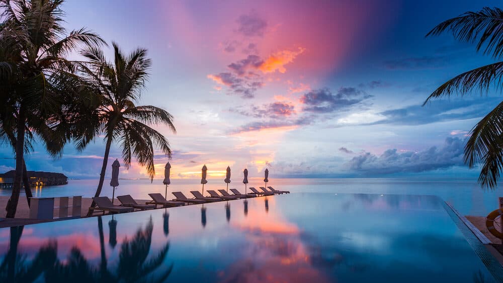 Luxury infinity pool overlooking sunset sea and sky reflection. Amazing swimming pool and beach background