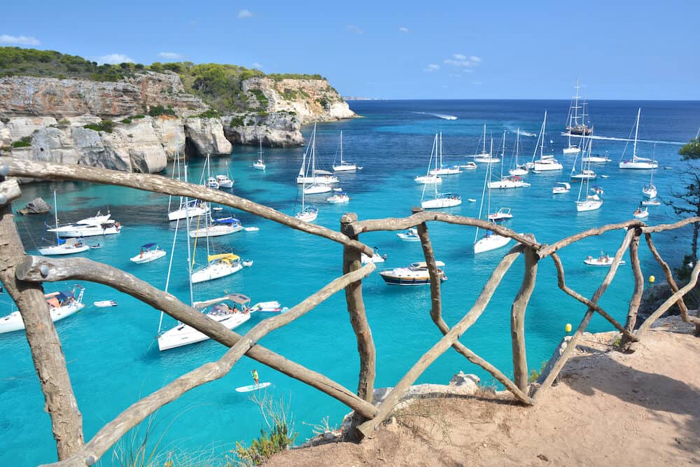 Turquoise water in bay Cala Macarella on Menorca island in Spain. Wooden typical fence.